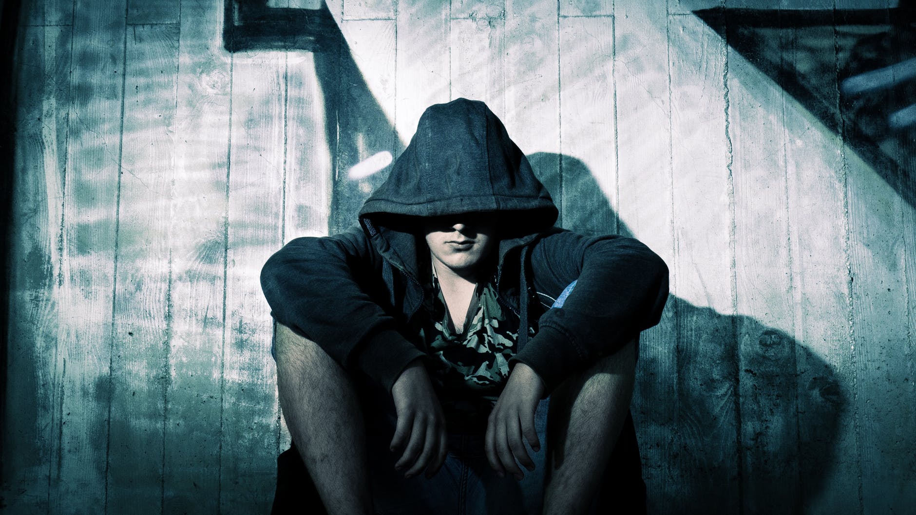 person wearing black zip hoodie sitting in front of gray wooden plank wall during nighttime